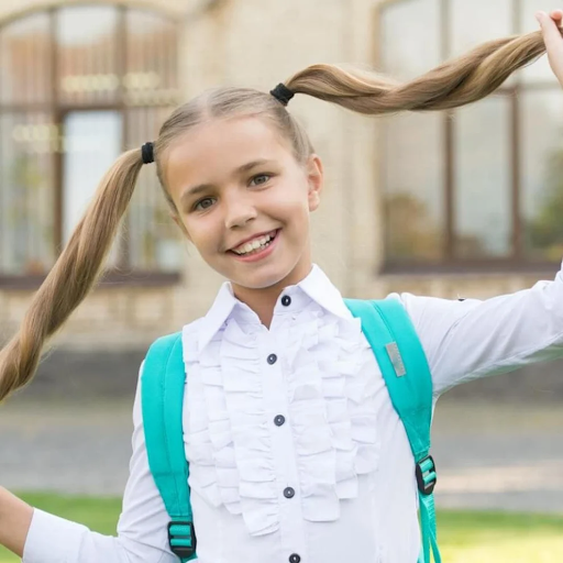 Smiling schoolgirl in pigtails tied with NatPat head lice repellent hair bands, wearing a teal backpack outside school.