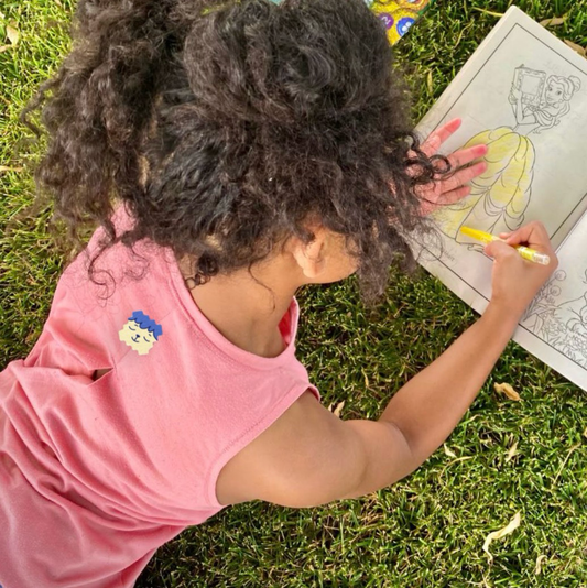Child wearing a NatPat ZenPatch sticker on a pink shirt, calmly coloring on grass to self-regulate.