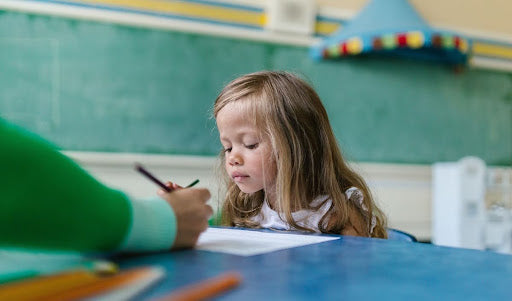 Young girl with long loose hair sitting close to a classmate at a school desk in a classroom.