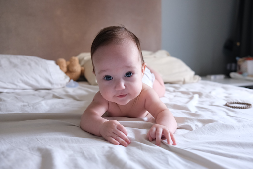Blue-eyed baby lying on a white bed, wearing a white diaper.