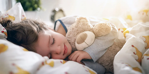 Young child sleeping peacefully in bed while hugging a stuffed teddy bear.
