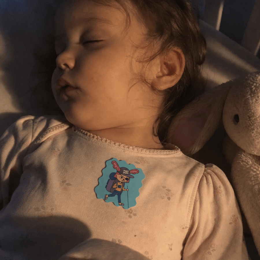 Parent tucking a sleeping child into bed, a StuffyPatch sticker visible on the child's pajama collar.