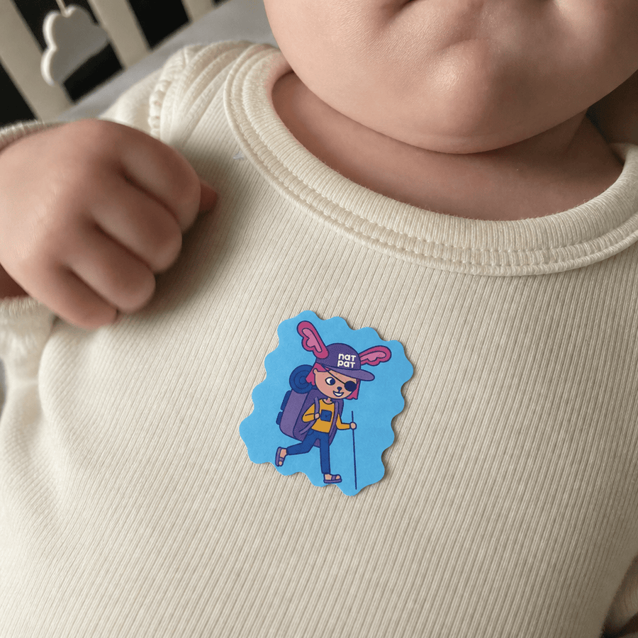 A caregiver applying a StuffyPatch sticker to a sleeping newborn's onesie collar.