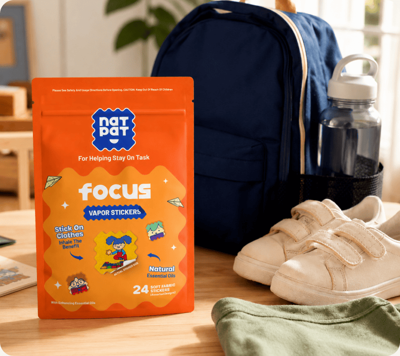 An orange NATPAT Focus Vapor Stickers pouch stands on a wooden desk beside a navy backpack, a water bottle and a pair of trainers.