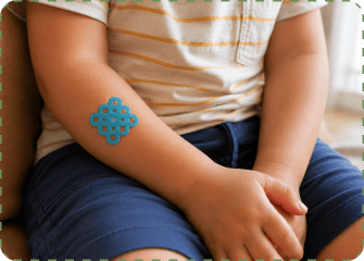 Close-up of a seated toddler in a striped shirt and jeans with a teal grid-shaped MagicPatch on the inside of their forearm, hands resting in their lap.