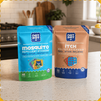 Two NatPat pouches stand side by side on a kitchen counter — the blue Mosquito Repellent Stickers pack and the tan Itch Relief Stickers pack.