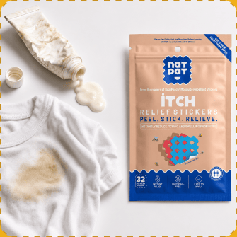 A squeezed, uncapped cream tube spills a blob of white cream beside a white t-shirt stained brown, next to a peach-and-blue NatPat ITCH Relief Stickers pouch.