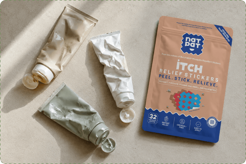 Three squeezed cream and gel tubes with their caps flipped open lie on a sunlit beige surface beside a peach-and-blue NatPat ITCH Relief Stickers pouch.