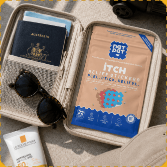 A NatPat Itch Relief Stickers pack tucked into an open travel document wallet beside an Australian passport, a pair of tortoiseshell sunglasses and a tube of sunscreen.