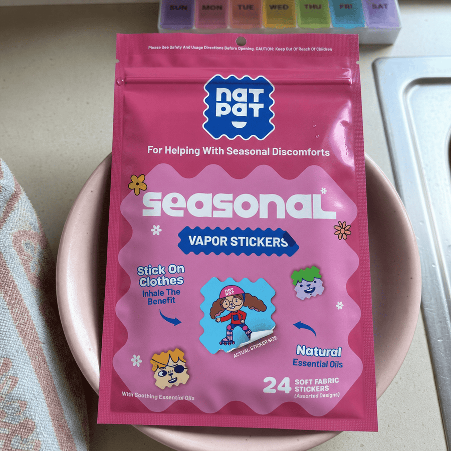 A pink pouch of NatPat Seasonal Vapor Stickers resting on a plate, showing the packaging and a soft-fabric sticker at actual size.