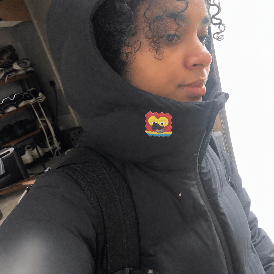 A woman wearing a hooded jacket with a colorful AllergyPatch sticker applied to the collar near her neck.