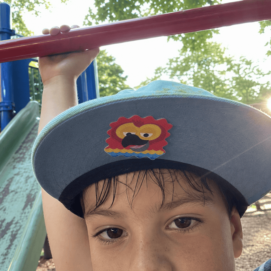A boy at a playground wearing a cap with a colorful sticker patch on the brim, gripping a red bar overhead.