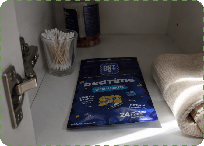 A NATPAT BedTime Vapor Stickers pack sitting on a bathroom cabinet shelf between a jar of cotton buds and a rolled white towel.