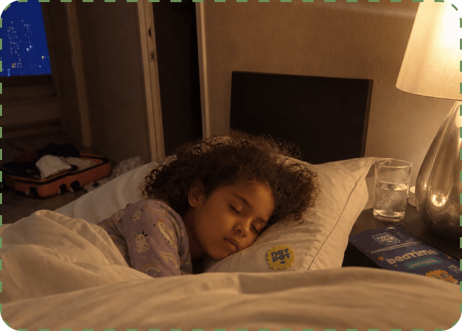 A young girl asleep on a white pillow in a dim hotel bedroom, a yellow NATPAT sticker on her pyjama sleeve, an open suitcase behind her and a Bedtime Vapor Stickers pouch on the bedside table.