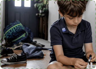 A boy with a ZenPatch sticker on his navy polo collar sits on the hallway floor playing quietly, his backpack, shoes and jacket dropped by the front door behind him.