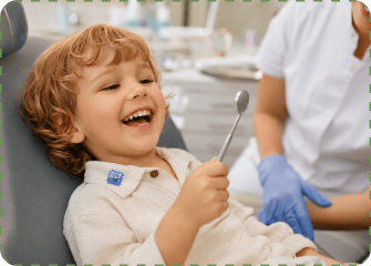A laughing curly-haired child with a blue NatPat sticker on their shirt collar reclines in a dentist's chair holding a dental mirror, with a dental professional in blue gloves beside them.