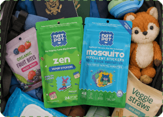 An open suitcase packed with a green NATPAT Zen Vapor Stickers pouch and a blue Mosquito Repellent Stickers pouch alongside a passport, organic fruit bites, veggie straws and a plush fox toy.